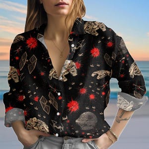 Op de afbeelding: Zwart overhemd met een Star Wars-thema. Het ontwerp bevat illustraties van ruimteschepen, rode uitbarstingen en de Death Star. Het shirt met lange mouwen heeft een kraag en is gemaakt van een lichte stof.