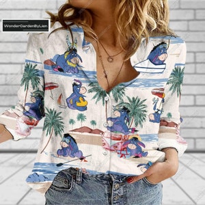 May include: A white button-down shirt with a tropical print featuring a blue donkey character in various beach scenes. The shirt has long sleeves and a relaxed fit.