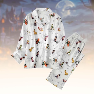 May include: A white long-sleeve pajama set featuring a button-down shirt and matching pants. The fabric is decorated with a repeating pattern of Disney characters in Halloween costumes, including Mickey and Donald, interspersed with spider webs.