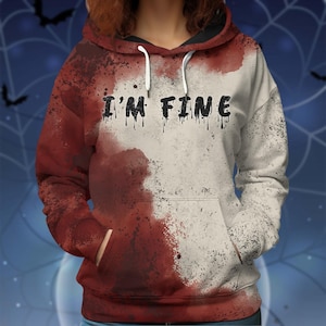 May include: A hooded sweatshirt with a distinctive design. The hoodie is split, with a red and white colour scheme. The words "I'M FINE" are printed across the chest in black, with a dripping effect. The hoodie has a front pocket and white drawstrings.
