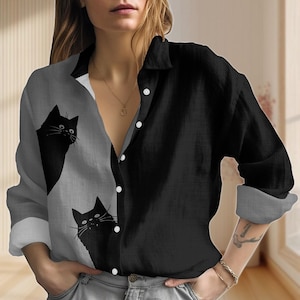 Peut inclure: Chemise boutonnée avec un design divisé : un côté noir, l'autre gris avec des graphiques de chats noirs. La chemise a un col et des manches longues. Des boutons blancs sont cousus sur le devant.