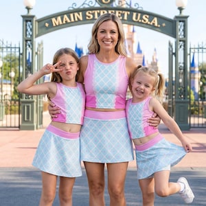 May include: Three matching two-piece outfits consisting of a sleeveless pink and light blue crop top and a coordinating skirt. The tops and skirts feature a light blue diamond lattice pattern with small pink dots, accented by solid pink trim.
