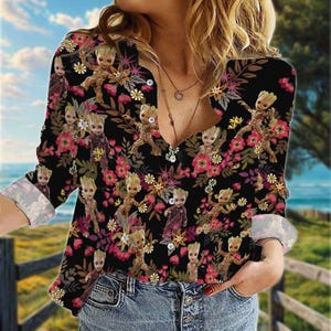 May include: A black long-sleeved button-up shirt with a floral print featuring a cartoon character. The shirt has a V-neck and a button-up front.