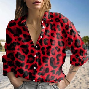 May include: A long-sleeved button-down shirt featuring a vibrant red and black leopard print pattern. The shirt has a classic collar, a front button placket with white buttons, and a relaxed fit, worn tucked into light gray denim jeans.
