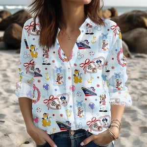 Op de afbeelding: Lichtblauwe button-down blouse met een Disney-thema print. De blouse heeft verschillende Disney-personages, waaronder Mickey Mouse, Donald Duck en Pluto, samen met nautische elementen zoals ankers en cruiseschepen. Lange mouwen.