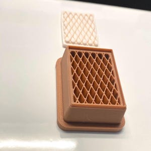 May include: A rectangular brown plastic cookie cutter featuring a diamond lattice grid pattern, accompanied by a separate white rectangular stamp piece that mirrors the same diamond grid design for creating textured impressions in dough.