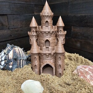 May include: A brown, detailed castle-shaped sandcastle toy with a pointed roof and multiple towers. The castle is sitting on a bed of sand with seashells scattered around it.