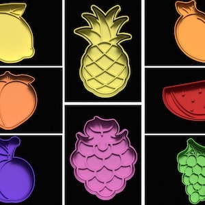 May include: Nine different cookie cutters in various fruit shapes, including a lemon, pineapple, peach, watermelon, blackberry, and grapes. The cutters are made of a light-coloured plastic and are arranged in three rows of three.