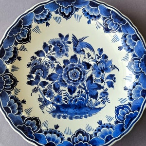May include: A blue and white Delftware plate with a floral design and a bird. The plate has a scalloped edge and is decorated with a traditional Dutch pattern.