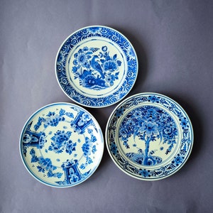 Può includere: Tre piatti in ceramica blu e bianca con intricati disegni floreali. I piatti presentano motivi tradizionali di Delftware olandese.