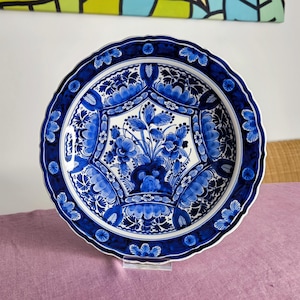 Könnte beinhalten: Ein großer blauer und weißer Keramikteller mit Blumenmuster. Der Teller hat einen gewellten Rand und ist mit einem zentralen Motiv aus Blumen und Blättern verziert.
