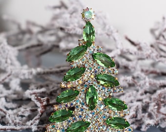 May include: A green rhinestone Christmas tree brooch with a sparkly finish. The brooch is made of clear and green rhinestones.
