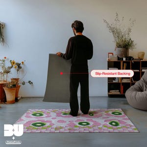 Person holding and showing the back of the rug with a slip-resistant backing showcase in a living room, highlighting a demonstration of the colorful pink flower, abstract leopard and green checkered area rug for the eclectic interior, dopamine decor.
