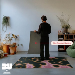 Person holding and showing the back of the rug with a slip-resistant backing showcase in a living room, highlighting a demonstration of the dark green, pink and yellow animal print faux tufted texture printed area rug for the eclectic home.