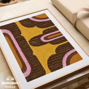 Wood-framed yellow, pink and brown eclectic retro rug art print— the geometric textile painting resembles a tufted rug texture textile wall art decor, Bauhaus poster placing on wood table for dorm room essentials.