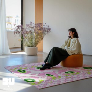 Woman sitting on a round single seat sofa in a modern, minimalistic living room, large potted flowers and a colorful geometric rug in maximalist home decor style, featuring pastel pink flower, green checkered and leopard pattern. 5x7 rug.