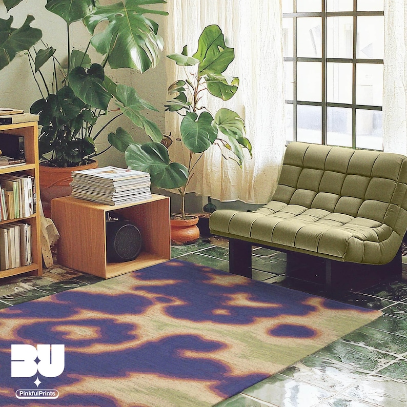 An eclectic abstract cowhide floral area rug is placed in a cool and cozy apartment, featuring books in cabinets, large houseplants, and sage green single sofa on green tiled floor. This rug showcases hand painted cowhide and floral patterns, embodying an aura and psychedelic style with vivid hues of purple, yellow, orange, and green. It’s perfect for dopamine home decor and aesthetic decor lovers.