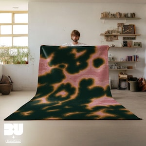 Person holding a dopamine decor, Pink Psychedelic Area Rug, with abstract animal print pattern, dark green yellow hues , standing in a cozy room with books and decor on shelves.