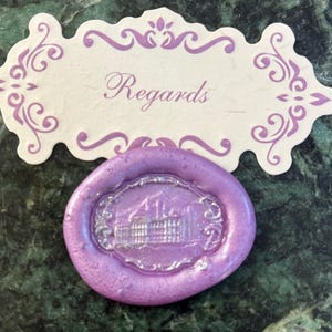 May include: A purple wax seal with a silver embossed design of a building. The seal is on a white card with the word "Regards" written in purple.