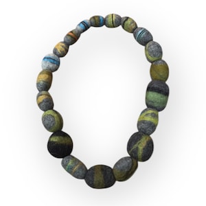 Puede incluir: Un collar artesanal con cuentas ovaladas de fieltro. Las cuentas son principalmente grises, con detalles en verde, amarillo, azul y naranja. El collar se muestra sobre un fondo blanco.