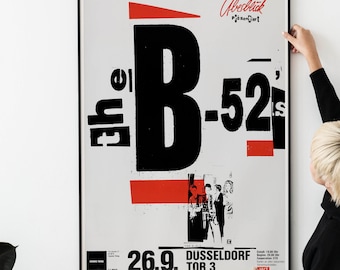 May include: A black and white poster with red accents advertising a concert by the B-52's. The poster features the band's name in large, bold letters and a smaller image of the band members. The concert is scheduled for June 26th at the Tor 3 in Dusseldorf, Germany.