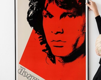 May include: A black and white portrait of Jim Morrison, the lead singer of The Doors, against a red background. The band's name, "THE DOORS", is printed in black at the bottom left corner of the poster.