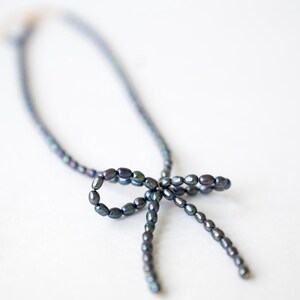 May include: A dark blue pearl necklace with a bow made of pearls.