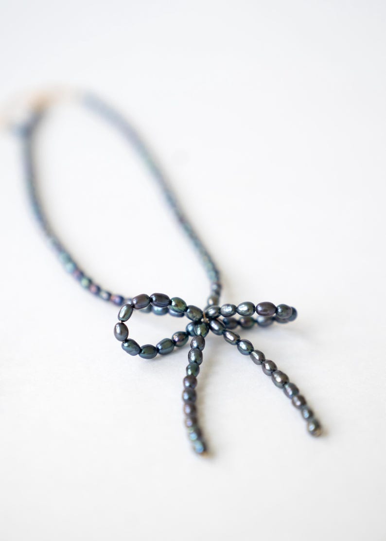 May include: A dark blue pearl necklace with a bow made of pearls.