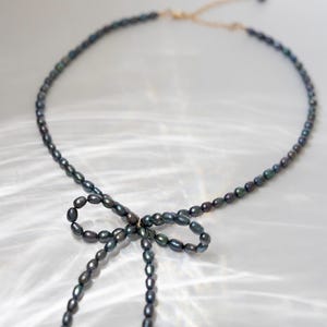 May include: A black pearl necklace with a bow made of pearls. The necklace is on a white background.
