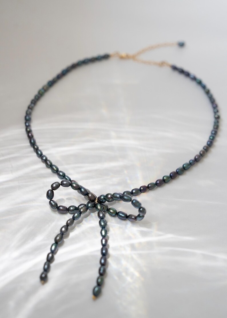 May include: A black pearl necklace with a bow made of pearls. The necklace is on a white background.