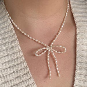May include: A delicate pearl necklace with a bow-shaped pendant. The necklace is made of small, white pearls and is tied in a bow at the center.