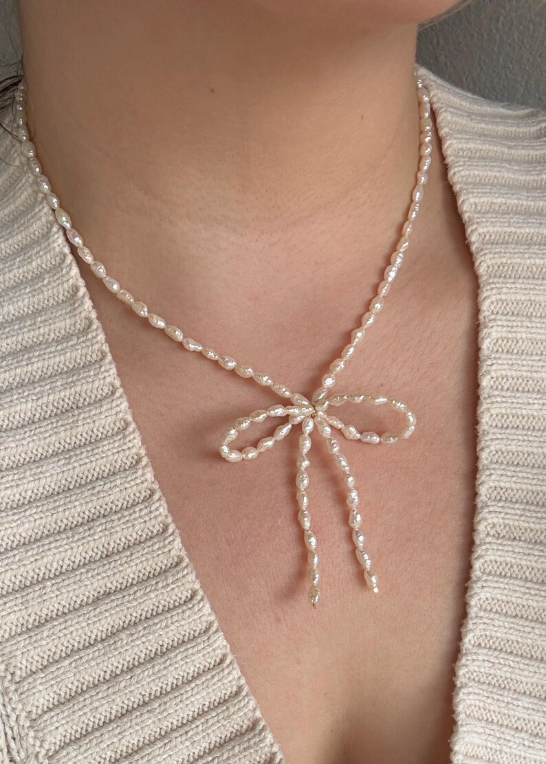 May include: A delicate pearl necklace with a bow-shaped pendant. The necklace is made of small, white pearls and is tied in a bow at the center.