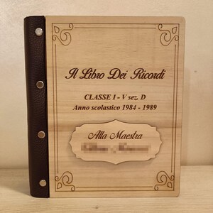 May include: A wooden memory book with a dark brown leather spine. The cover is engraved with the text "Il Libro Dei Ricordi", "CLASSE I-V sez. D", "Anno scolastico 1984-1989", and "Alla Maestra". The book has decorative corner designs.