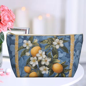 Op de afbeelding: Een blauwe en witte toilettas met een bloemen- en citrusontwerp. De tas heeft een herhalend patroon van citroenen, bloemen en bladeren.