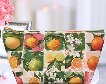 May include: A white zippered pouch with a colorful citrus fruit print. The pouch features lemons, limes, oranges, and grapefruit, along with green leaves and white flowers.