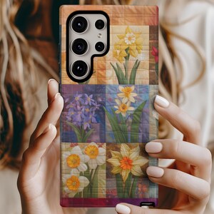 May include: A phone case with a colorful floral pattern. The case features a patchwork design with different types of flowers, including daffodils, in shades of yellow, white, and purple. The case has a black camera cutout and a black border.