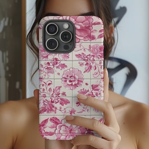 May include: A white phone case with a pink floral pattern. The case has a grid pattern and features a repeating floral design.