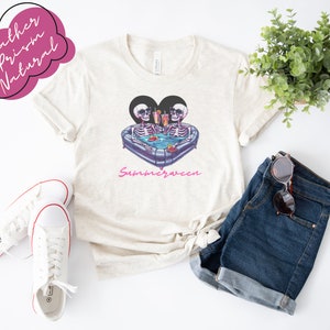 May include: A white t-shirt with a graphic of two skeletons in a heart-shaped inflatable pool with drinks. The text "Summerween" is printed below the graphic.