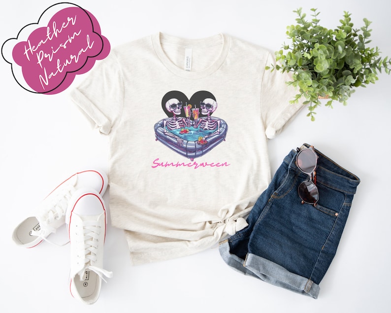 May include: A white t-shirt with a graphic of two skeletons in a heart-shaped inflatable pool with drinks. The text "Summerween" is printed below the graphic.