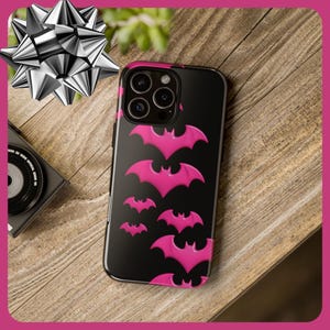 May include: Black phone case with a pink bat pattern. The case has a camera lens cutout and a black background.