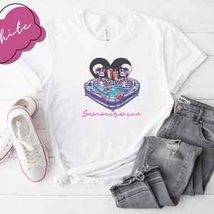 May include: White t-shirt with a graphic of two skeletons in a heart-shaped inflatable pool with the text "Summerween" underneath.