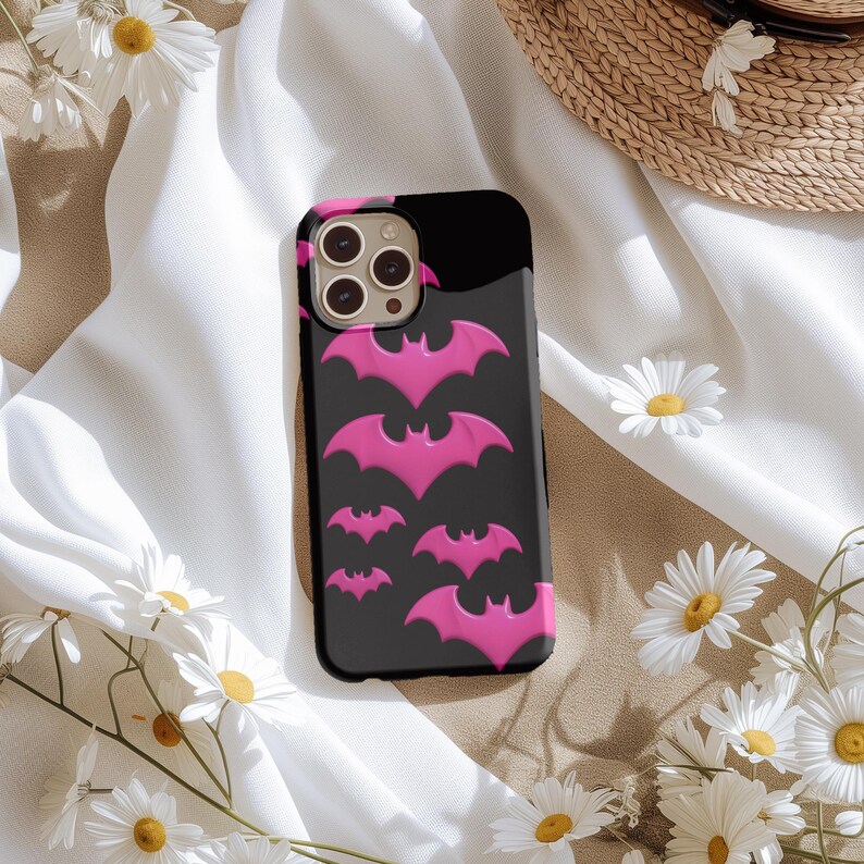 May include: A black phone case featuring a pink bat design. The case has a camera lens cutout and a black background.