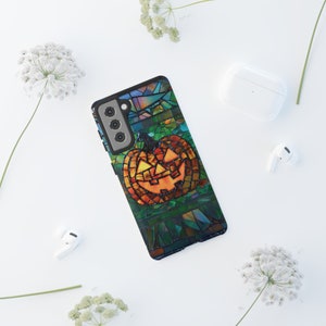 May include: A stained glass style phone case with a jack-o-lantern pumpkin design. The pumpkin is orange with a black face and is surrounded by green, blue, and purple glass pieces.
