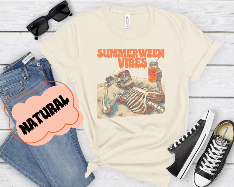 May include: A beige t-shirt with a graphic of a skeleton wearing sunglasses and holding a glass of iced tea. The text "Summerween Vibes" is printed in orange above the skeleton.