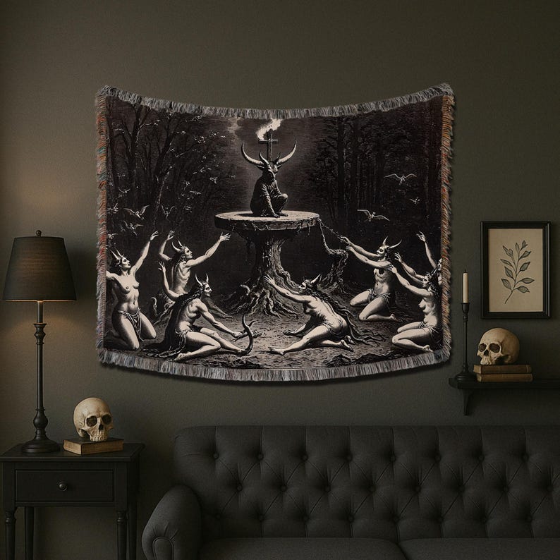 A black and white tapestry with a gothic theme. The tapestry features a central image of a demon with horns and a tail, standing on a platform with a burning torch. There are five figures surrounding the demon, all with horns and tails. The tapestry has a fringed border and is hung on a dark gray wall.