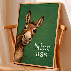 Könnte beinhalten: Gerahmter Kunstdruck mit einer Esel-Illustration auf grünem Hintergrund. Der Esel ist braun und weiß, mit einem humorvollen Ausdruck. Der Text "Nice ass" ist weiß geschrieben. Der Rahmen ist aus hellem Holz.