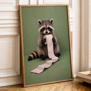 May include: A framed print featuring a raccoon holding a roll of toilet paper against a green background. The raccoon is depicted in realistic detail, with gray and brown fur and a black mask. The frame is a light brown color.