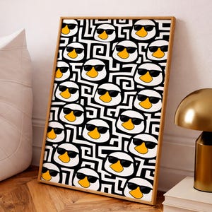 Può includere: Una stampa artistica incorniciata con un motivo ripetuto di facce di anatra bianche con occhiali da sole neri e becchi gialli, su uno sfondo a labirinto in bianco e nero. La cornice è di colore marrone chiaro. L'opera d'arte è esposta su una parete bianca.