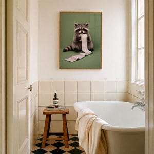 May include: A framed print featuring a raccoon holding a roll of toilet paper against a green background. The raccoon is depicted in shades of gray and brown, with a black mask and striped tail. The print is displayed in a bathroom setting with a white bathtub and a wooden stool.