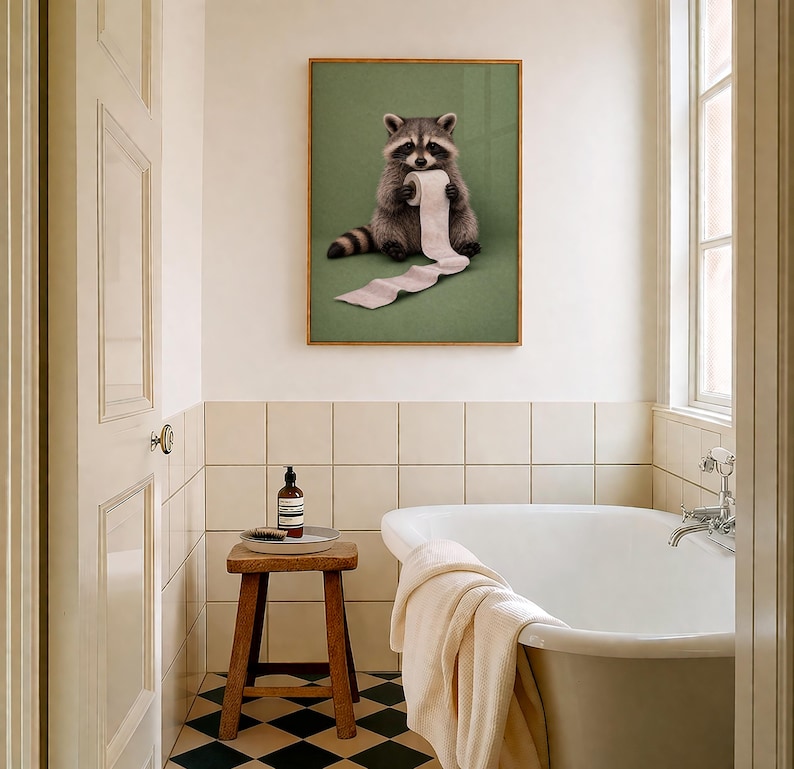 May include: A framed print featuring a raccoon holding a roll of toilet paper against a green background. The raccoon is depicted in shades of gray and brown, with a black mask and striped tail. The print is displayed in a bathroom setting with a white bathtub and a wooden stool.